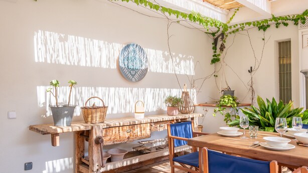 A dining area with a wooden table set for two, a rustic bench, and a wall-mounted decorative plate. - Villa 'Es Tancat' with Sea View, Private Pool and Wi-Fi (Sa Ràpita)