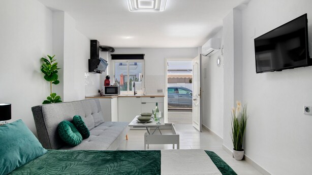 Un salon moderne avec un canapé, une table à manger et un coin cuisine visible à travers une porte ouverte.