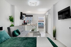 Un salon moderne avec un canapé, une table à manger et un coin cuisine visible à travers une porte ouverte.