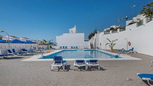 Une piscine avec des chaises longues, un bâtiment blanc et un ciel bleu azur.