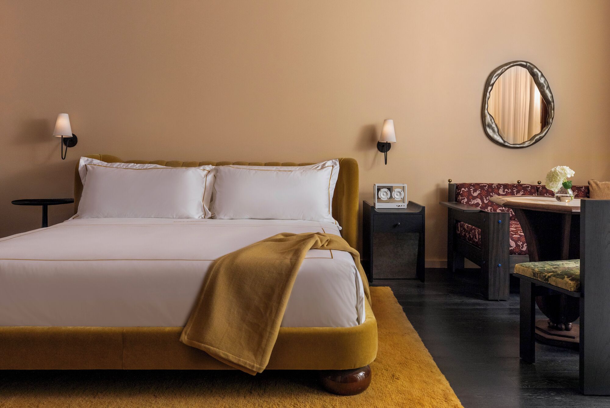 A hotel room with a bed, bedside tables, a desk with a chair, and a mirror on the wall.