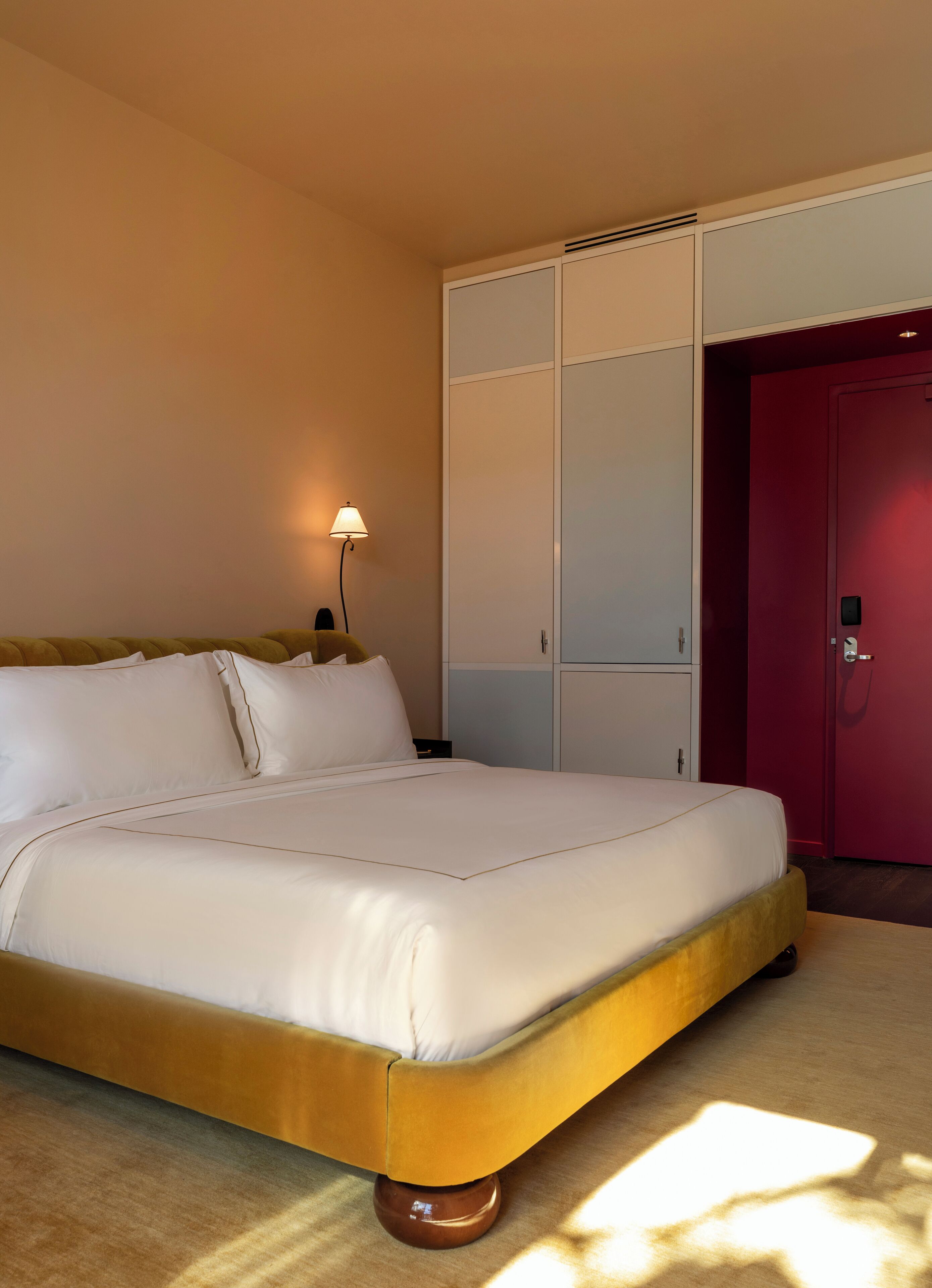 A neatly made bed with white linens, a bedside lamp, and a wardrobe with sliding doors.