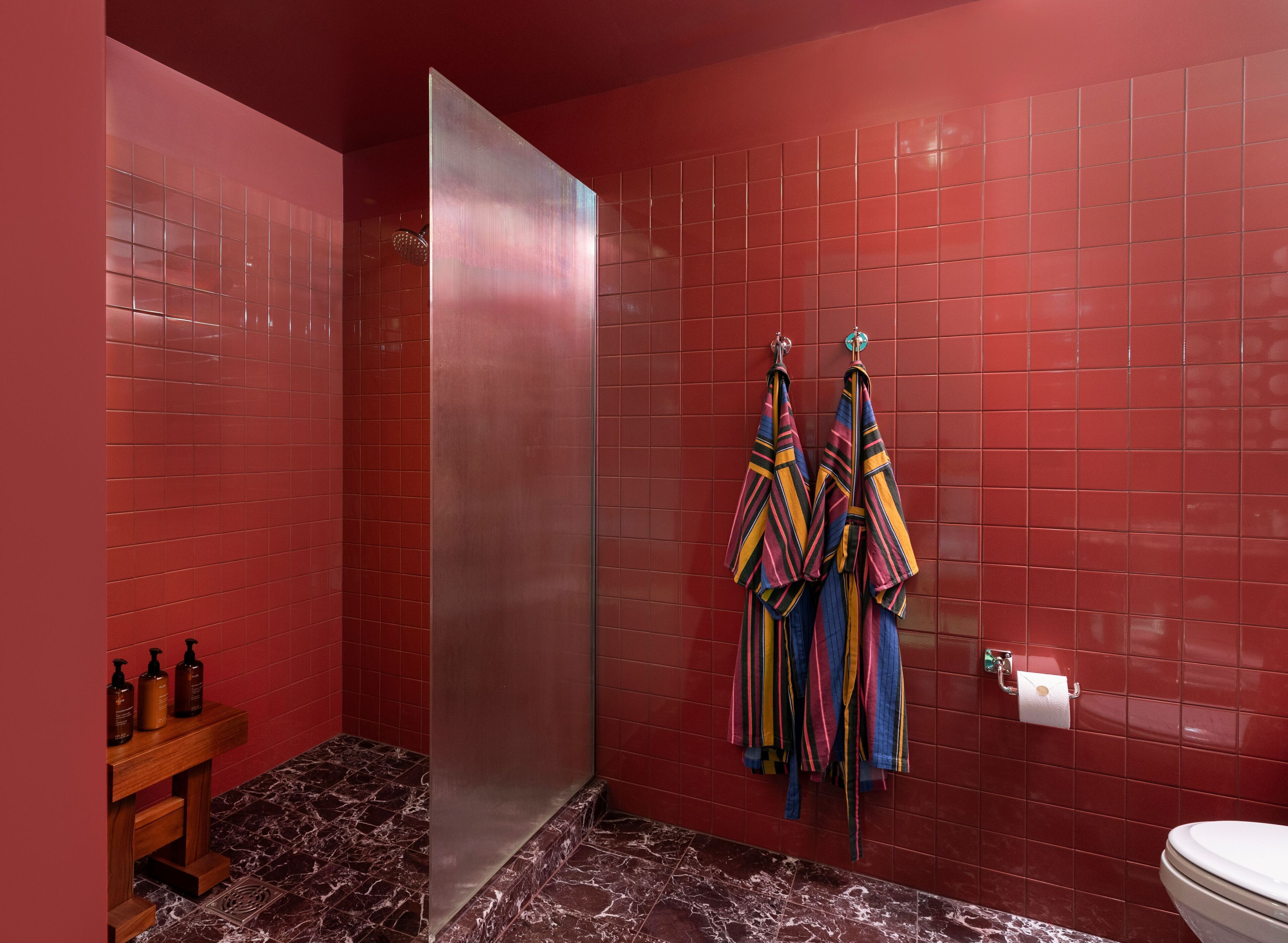 A bathroom with red tiled walls, a marble floor, a glass shower enclosure, and a toilet.