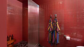 A bathroom with red tiled walls, a marble floor, a glass shower enclosure, and a toilet.