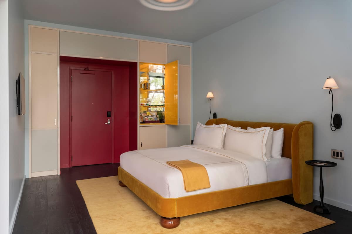 A bedroom with a bed, a red door, a wardrobe, and two wall-mounted lamps.