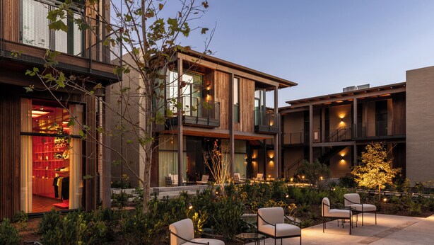 A modern building with multiple floors, large windows, and outdoor seating area with chairs and tables. - Hotel Saint Augustine (Houston)