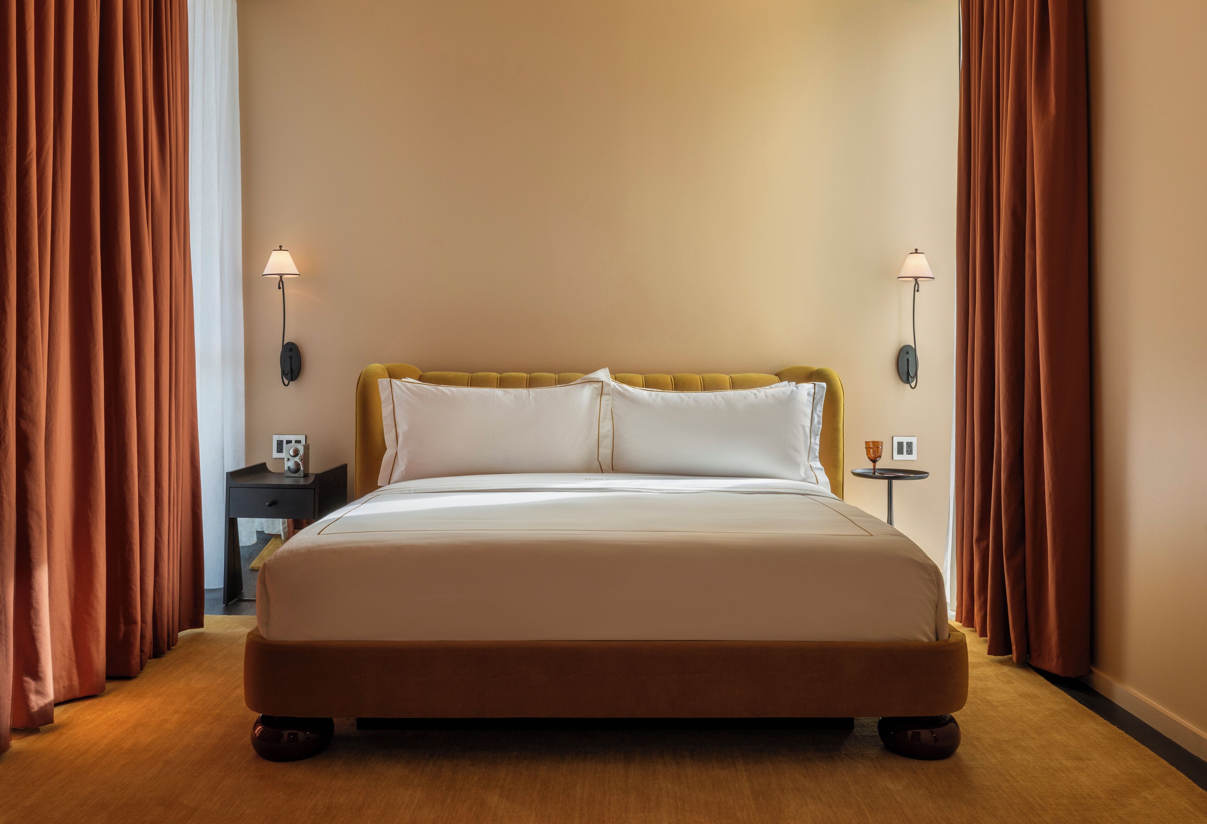 A hotel room with a large bed, two bedside lamps, a small table with a cup, and curtains.