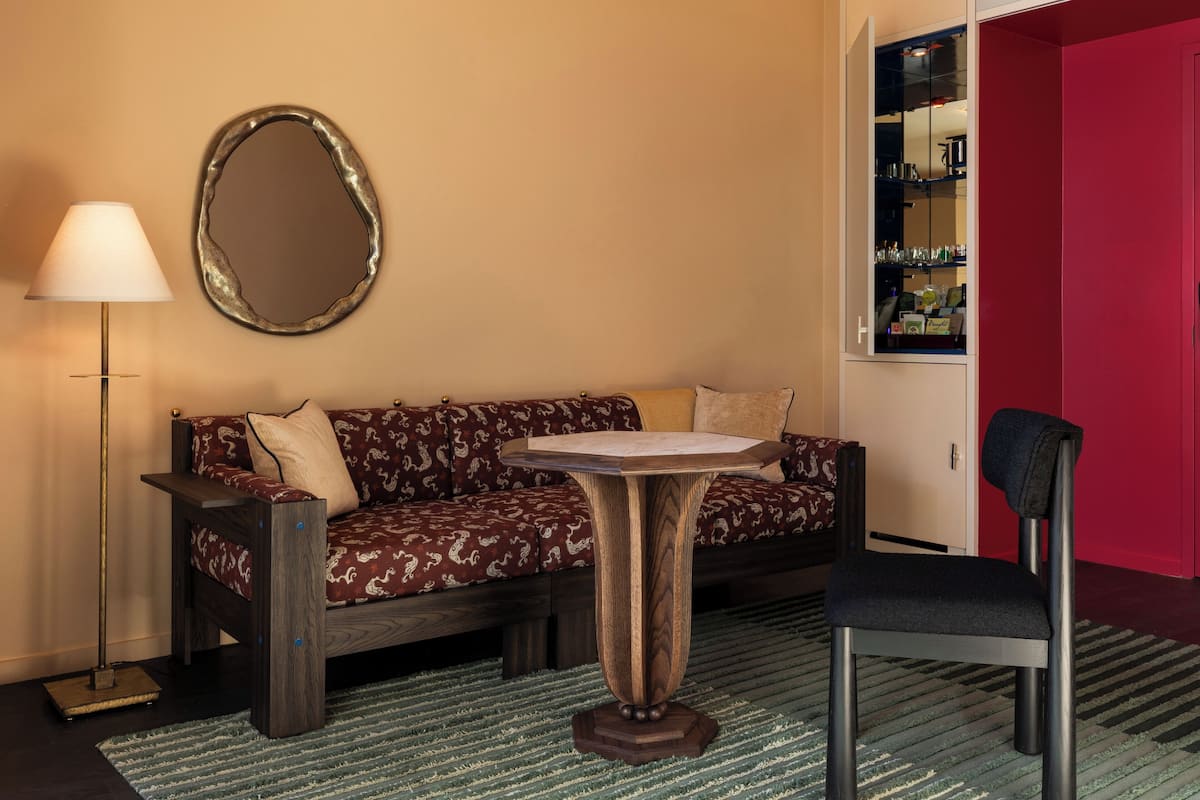 A room with a sofa, a small round table, a chair, a floor lamp, and a mirror.