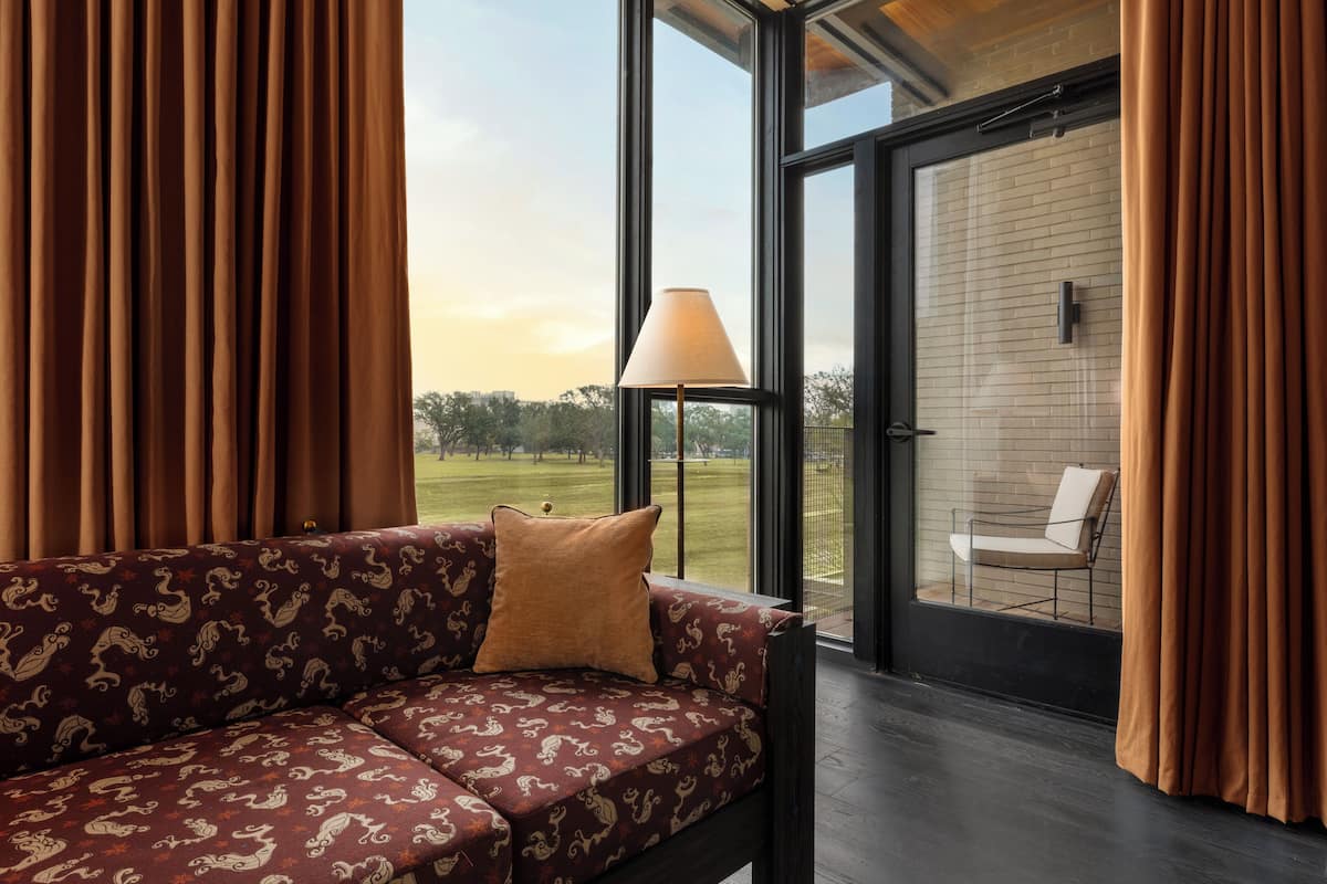 A modern living room with a patterned sofa, a floor lamp, and a view of a brick wall and outdoor seating area.