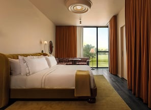 A hotel room with a large bed, a sofa, a small table, and a view of the outdoors through a sliding door.