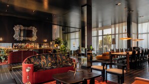 A modern lounge area with a bar, seating, and large windows. - Hotel Saint Augustine (Houston)