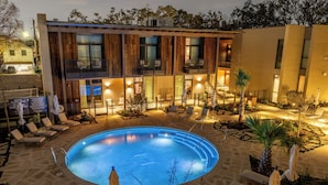 A modern building with a swimming pool, outdoor seating, and a well-lit patio area. - Hotel Saint Augustine (Houston)