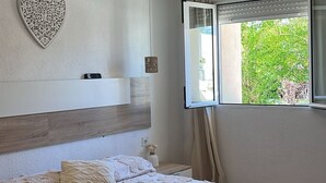 A bedroom with a large bed, a ceiling fan, a heart-shaped wall decoration, a window with curtains, and a view of greenery outside. - Masia Bernat: Antigua Masía en la Naturaleza Para Grupos (Tortosa)