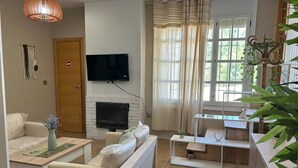 A living room with a fireplace, a television mounted on the wall, a sofa, a coffee table, and a dining area with a table and chairs. - Masia Bernat: Antigua Masía en la Naturaleza Para Grupos (Tortosa)