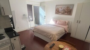 Ein kleines Schlafzimmer mit einem Bett, einer kompakten Küchenzeile und einem runden Holztisch.