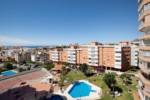 Un edificio moderno con molti balconi, una piscina e un campo da tennis.