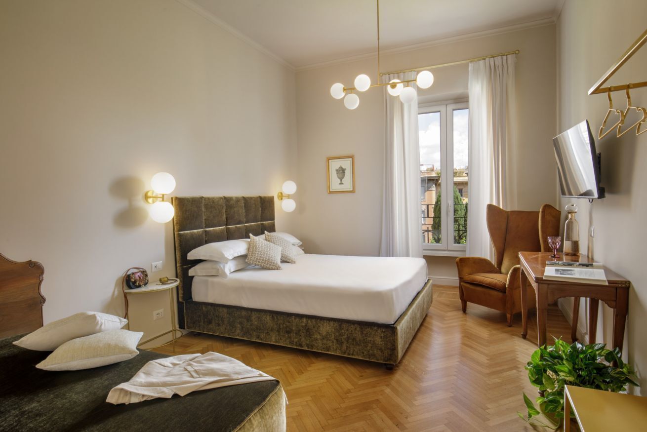 A hotel room with a large bed, a desk, a chair, a TV, and a window with curtains.