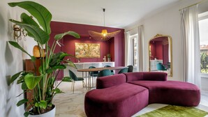 A modern living room with a sectional sofa, a dining area with a table and chairs, a large potted plant, and a painting on the wall.