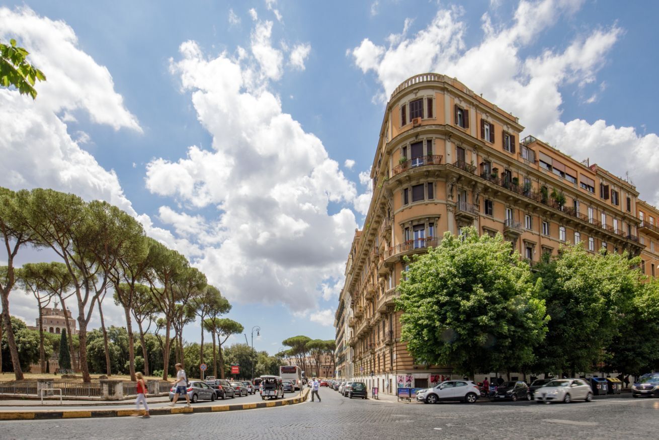 Un immeuble à plusieurs étages doté d’une façade incurvée, avec des voitures garées et des arbres le long de la rue.