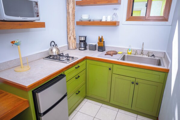 A kitchen with green cabinets, a microwave, a kettle, a coffee maker, and a sink. - Lagoonfront 1BR Oasis Unit A – Gated, Private, 10 Min from Belize Airport & City (Belize City)