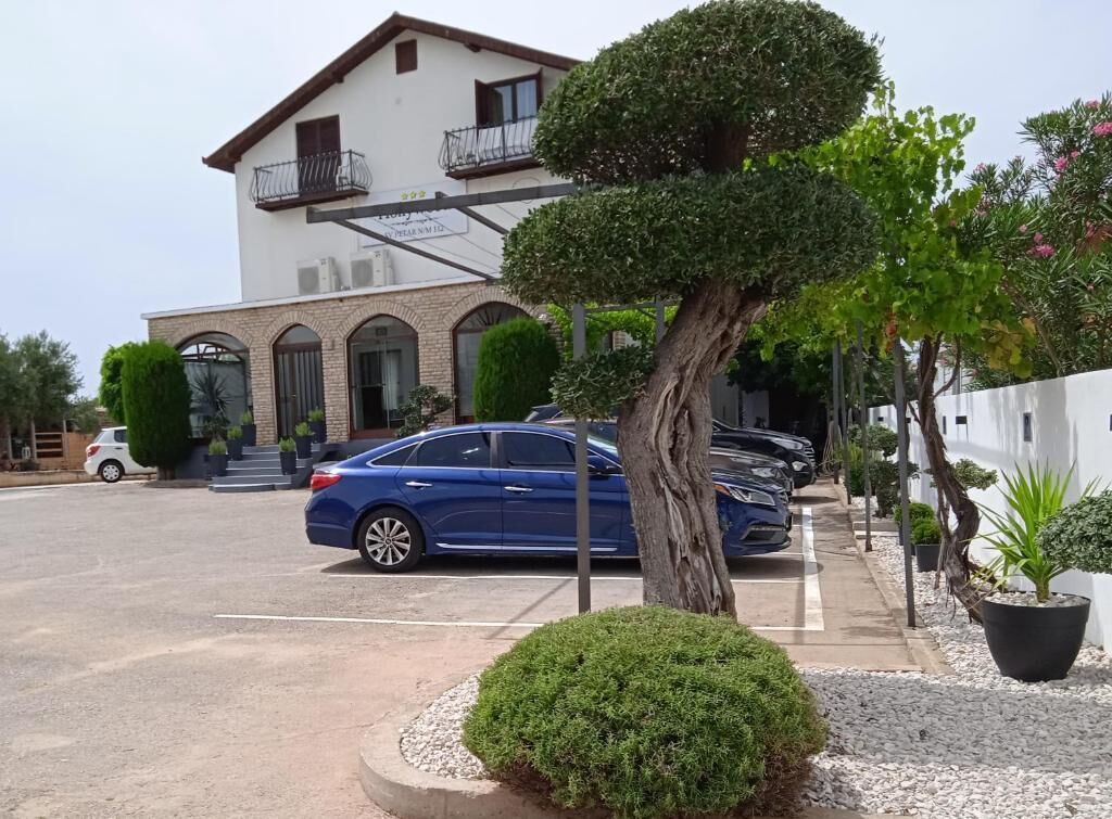 Un edificio de dos plantas con balcón, coches aparcados y un jardín bien cuidado.