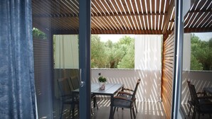 Een balkon buiten met een tafel, stoelen, een houten pergola en uitzicht op bomen.