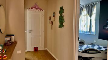 Ein Zimmer mit Holzboden, einer weißen Tür, einem kleinen roten Stuhl, einem Tisch mit Spielzeug und einem Automodell.