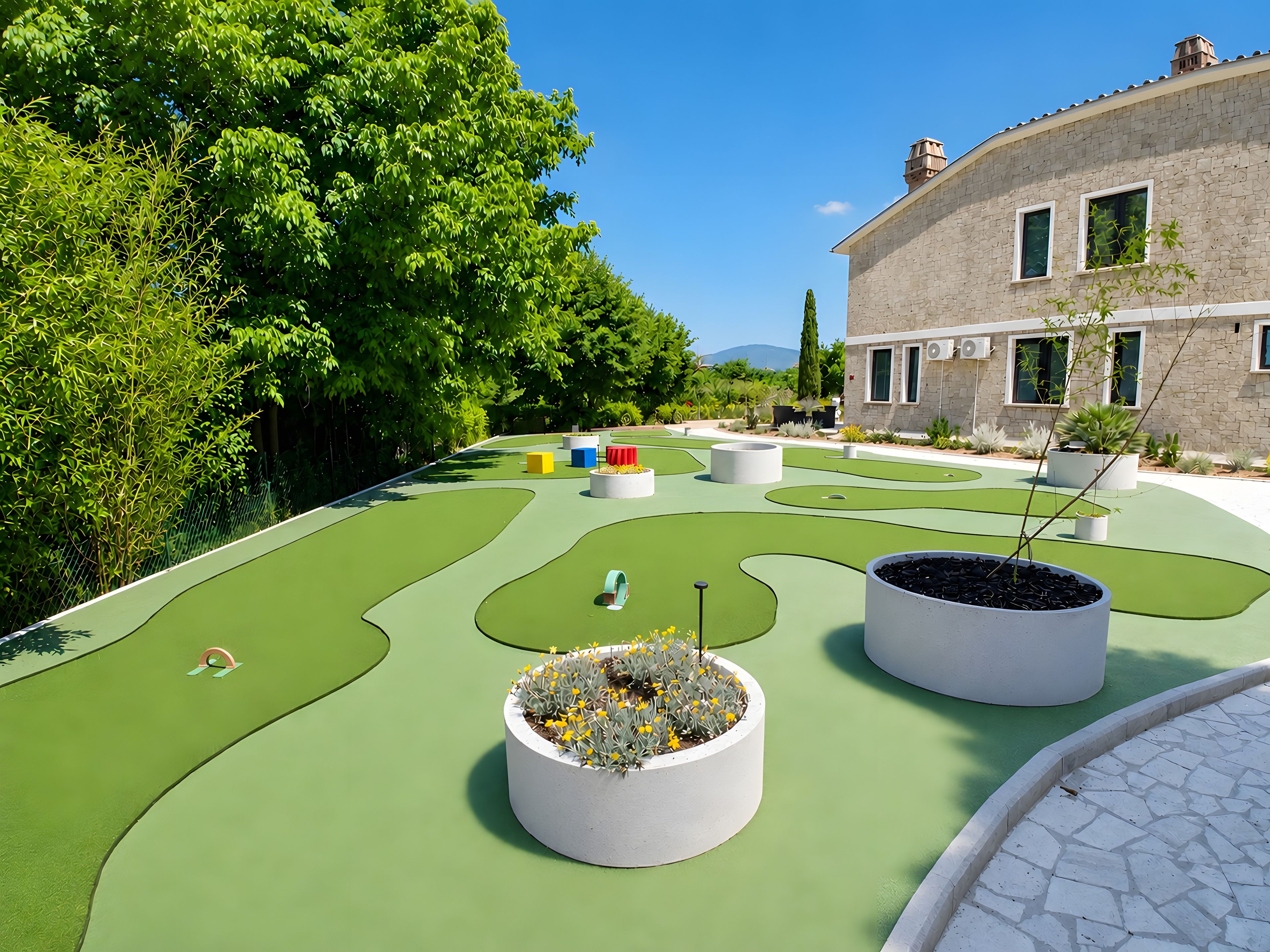 Un campo da minigolf con superficie verde, fioriere bianche con piante e un edificio con finestre sullo sfondo.
