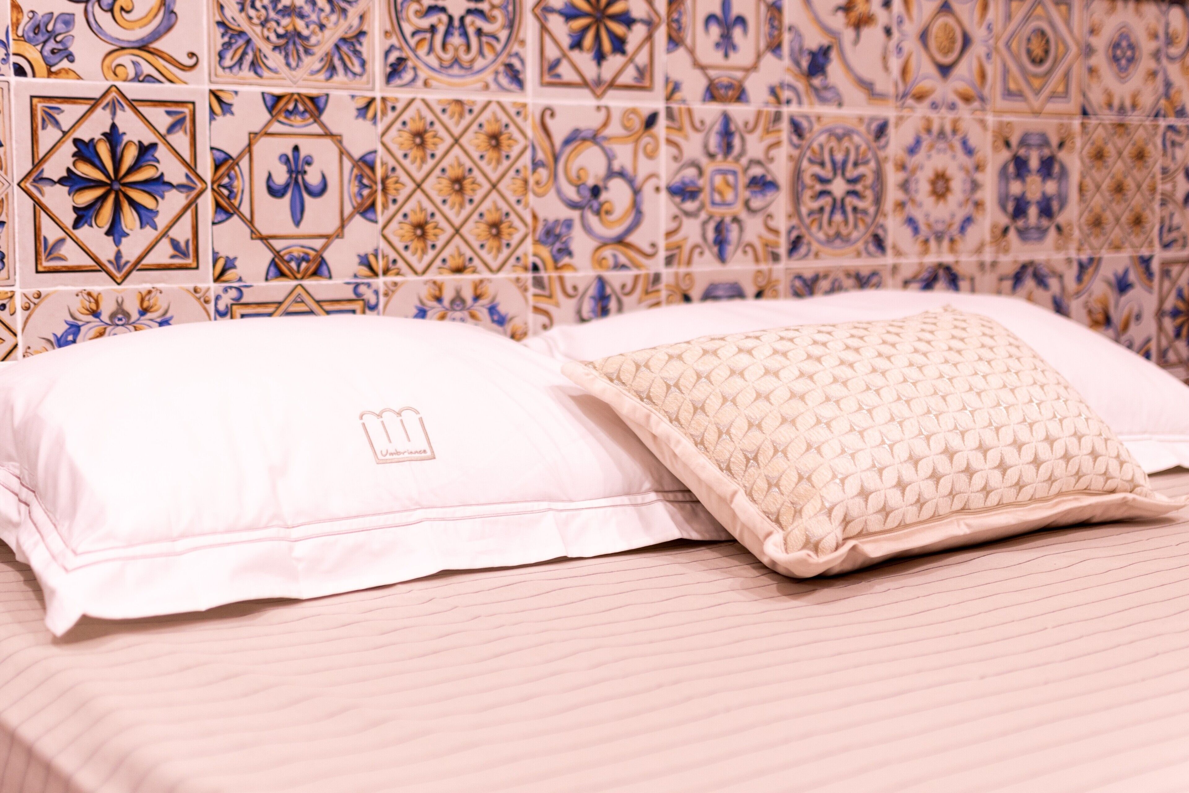 Un lit avec deux oreillers, un mur décoré d’un motif et un sol carrelé.