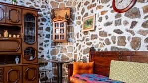 A room with a stone wall, wooden furniture, a bed with colorful bedding, a small table, and a clock. - Country House 'Casa Rural Del Tormes' with Mountain View, Private Terrace and Private Garden (Puente del Congosto)