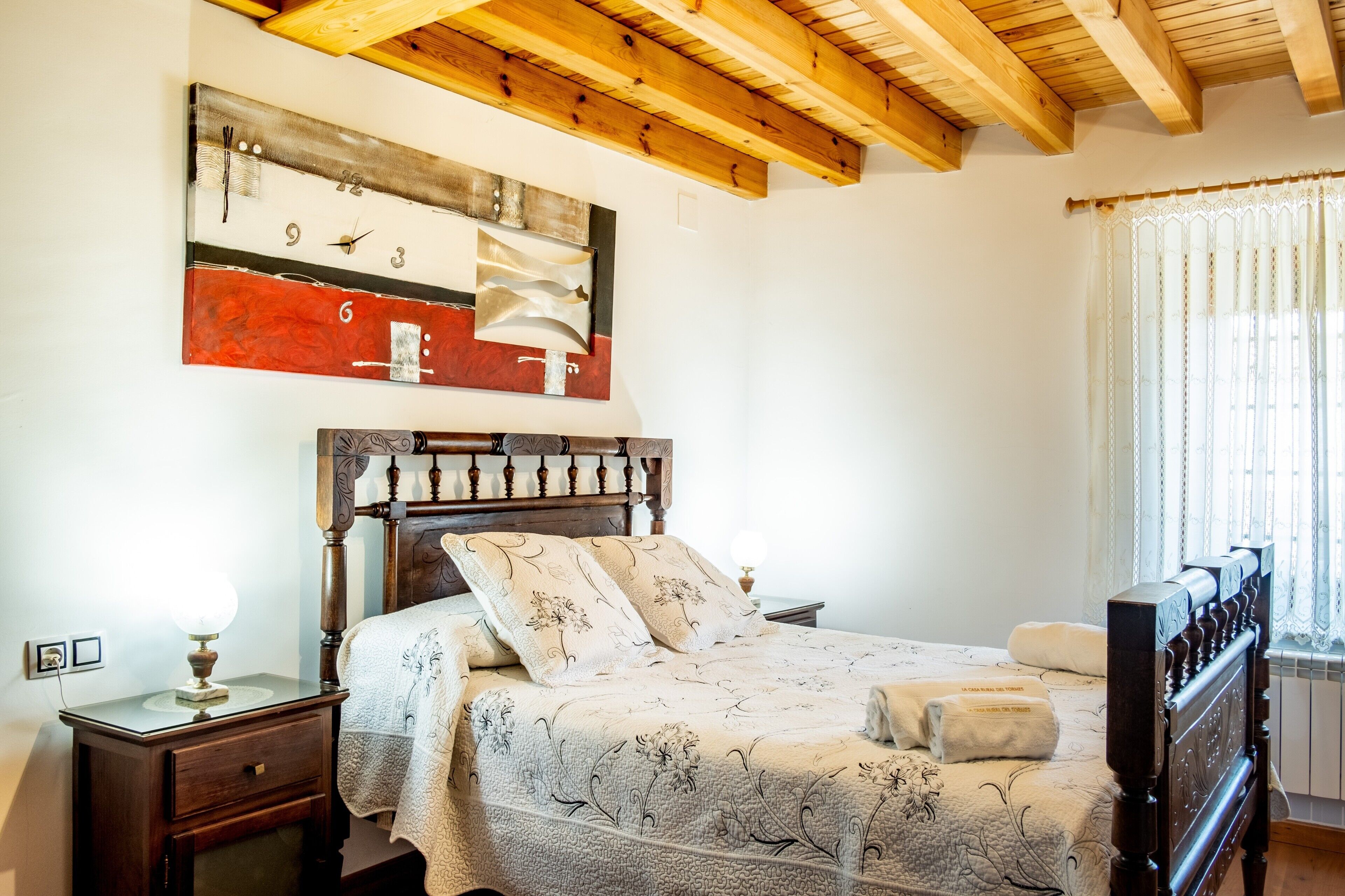 Une chambre à coucher avec un lit en bois, une table de chevet, une horloge murale et une fenêtre avec des rideaux.