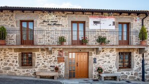 A stone building with a wooden door, windows, and a balcony with potted plants. - Country House 'Casa Rural Del Tormes' with Mountain View, Private Terrace and Private Garden (Puente del Congosto)
