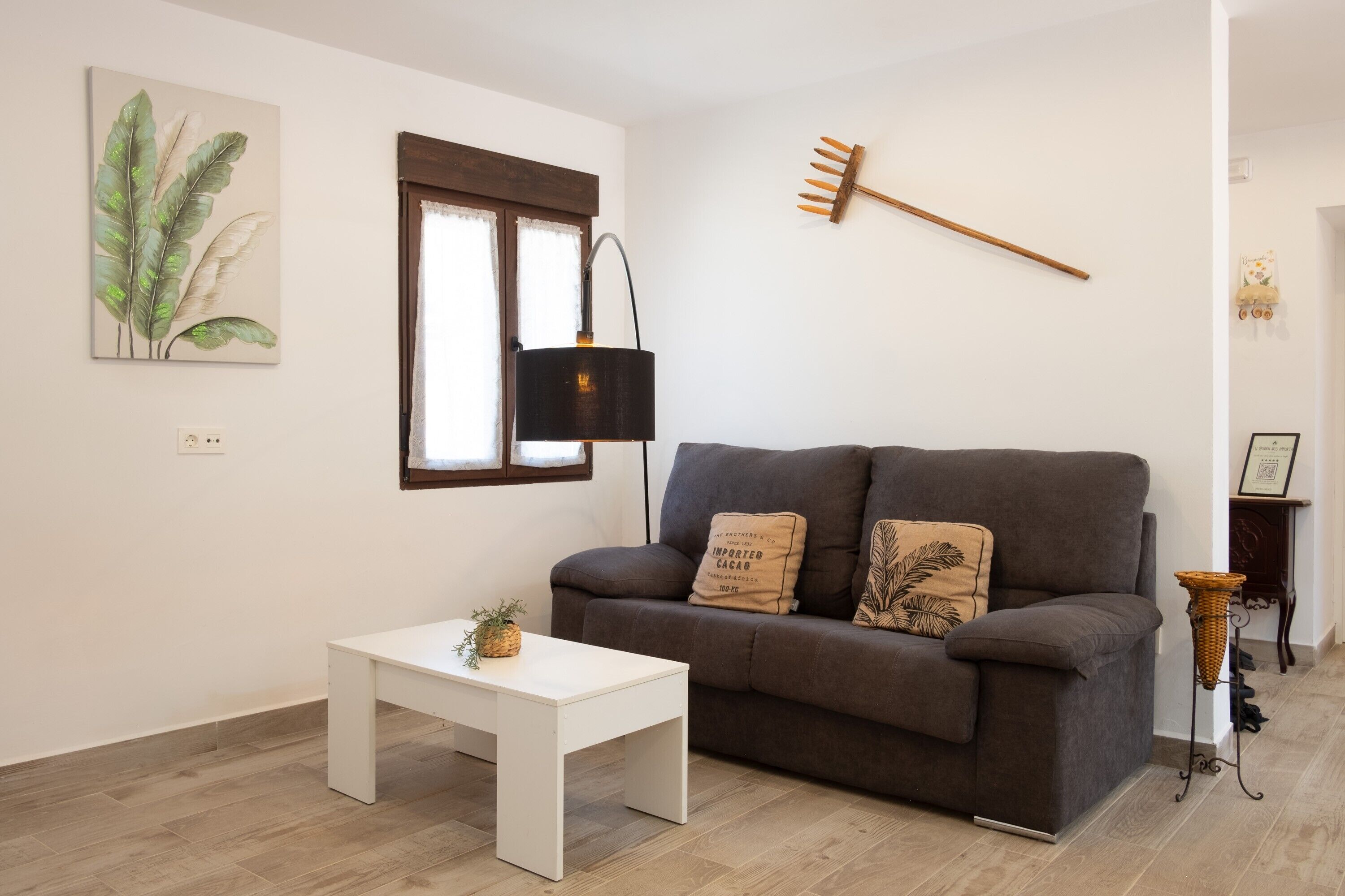 Een woonkamer met een grijze bank, een witte salontafel, een zwarte vloerlamp en een aan de muur bevestigde plant.