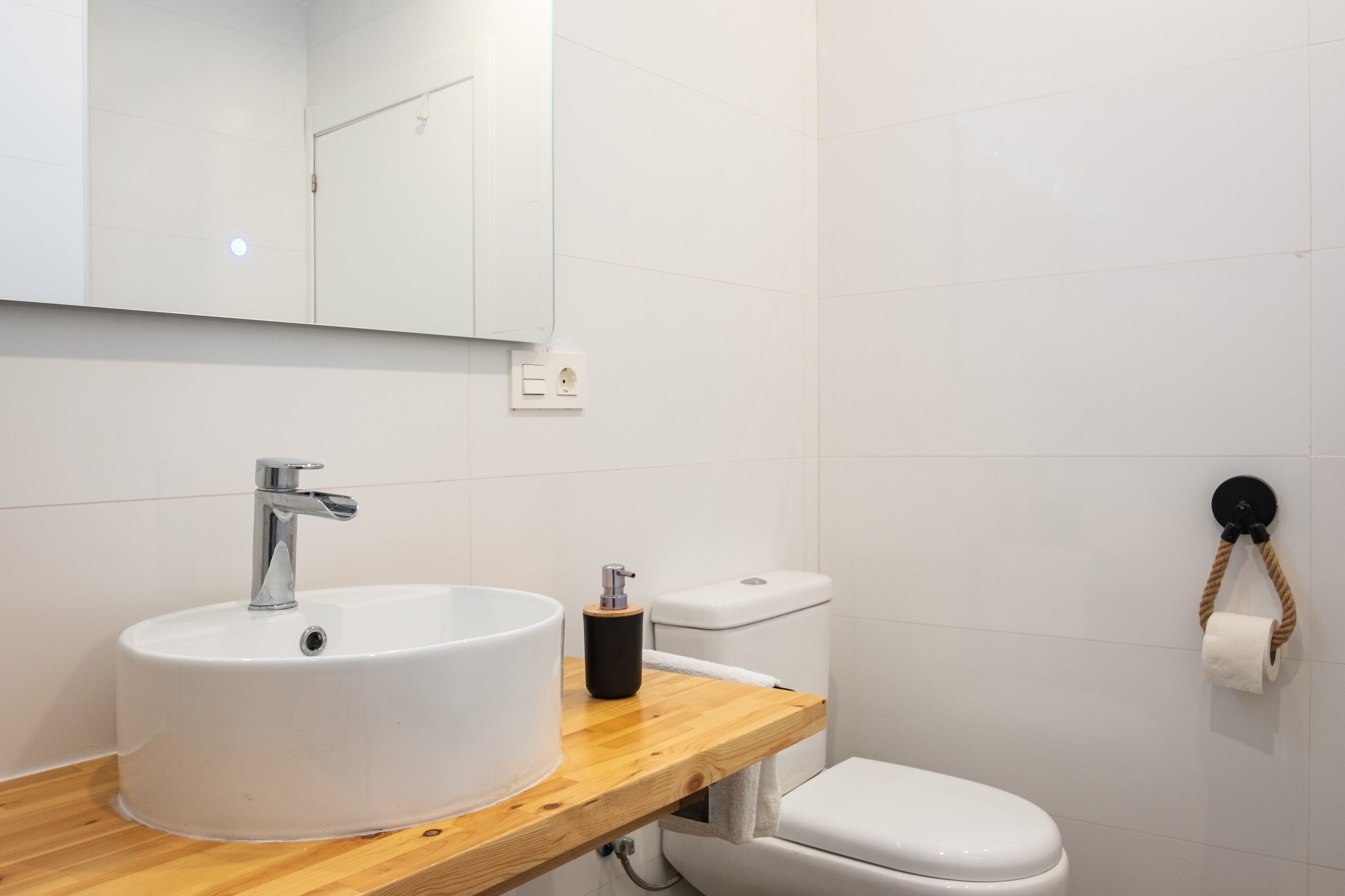 Un baño con lavamanos blanco, un espejo, un inodoro y un perchero para toallas.