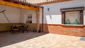 Une terrasse avec une table et des chaises, un mur en briques et une fenêtre ornée de bouteilles décoratives.
