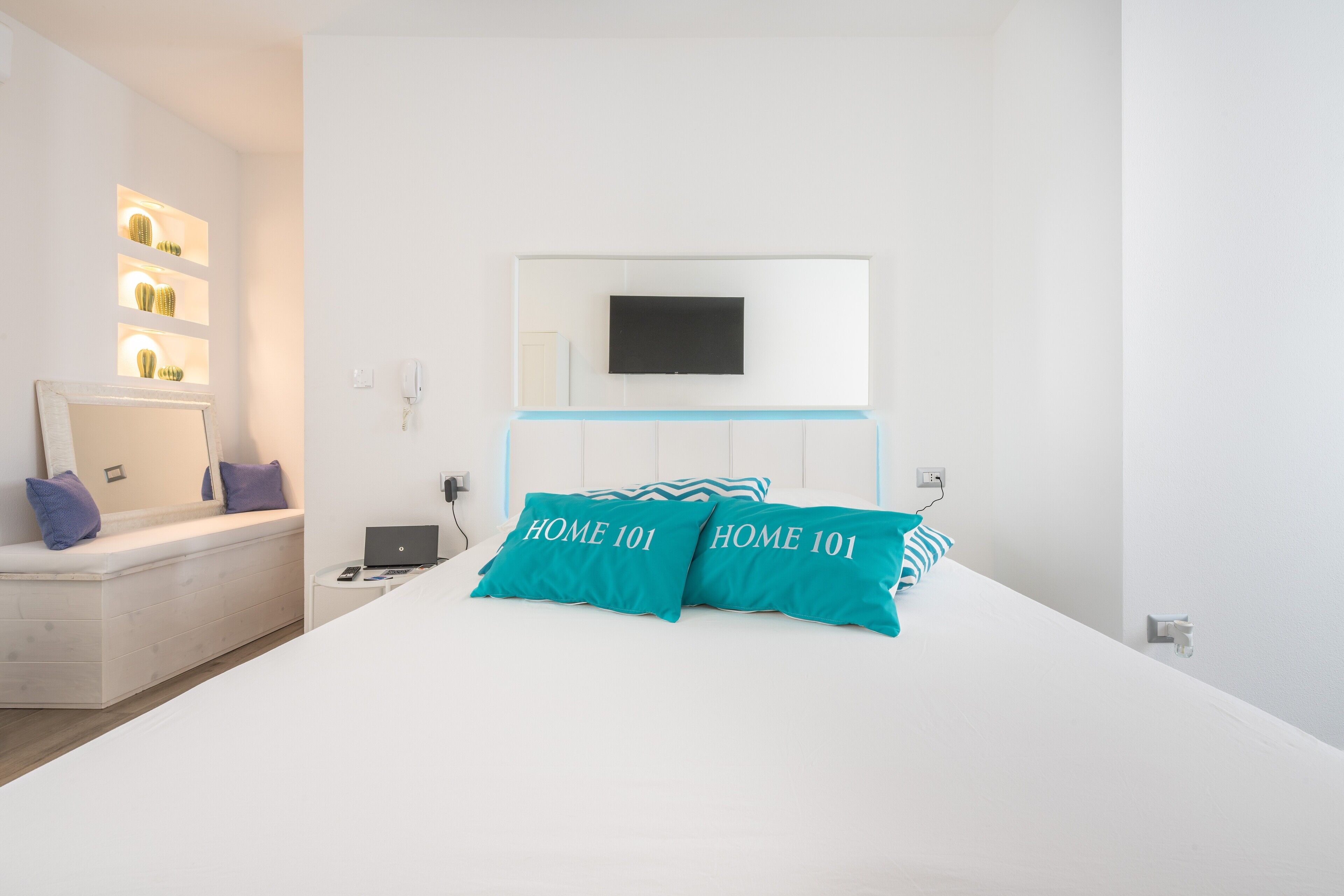 Ein Schlafzimmer mit Bett, einem an der Wand montierten Fernseher, einem Nachttisch mit Laptop und einem Beistelltisch mit Telefon.
