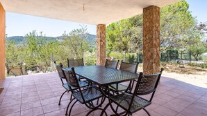 Un patio al aire libre con una mesa y sillas, rodeado de pilares de piedra, con vistas a un paisaje montañoso.