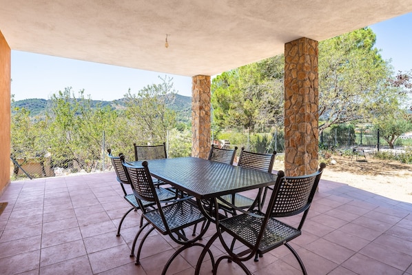 Un patio al aire libre con una mesa y sillas, rodeado de pilares de piedra, con vistas a un paisaje montañoso.