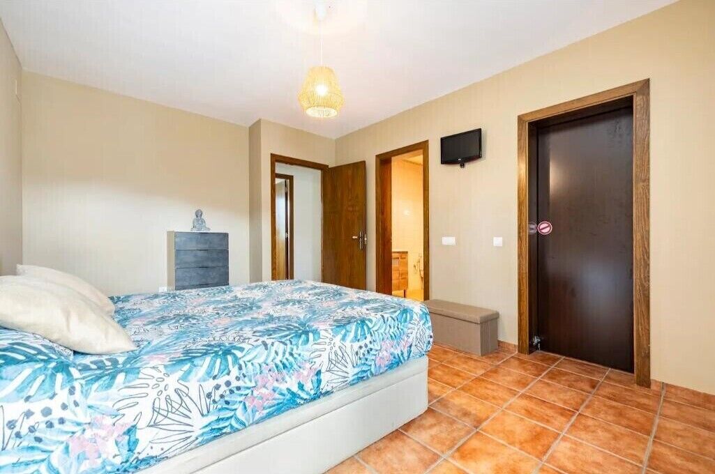 Un dormitorio con cama, mesita de noche, televisor y puerta.