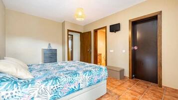 Un dormitorio con cama, mesita de noche, televisor y puerta.