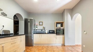 Una cocina moderna con electrodomésticos de acero inoxidable, armarios de madera clara y suelo de baldosas.