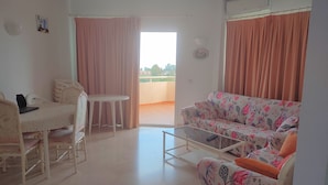 Un soggiorno con divano, tavolo, sedia e un balcone con tende.