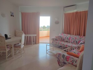 Een woonkamer met een bank, een tafel, een stoel en een balkon met gordijnen.