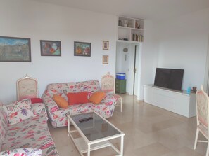 A living room with a sofa, a glass coffee table, a television, and a bookshelf.