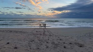 Ein Strand mit Fußspuren, die zum Wasser führen, ein klarer Himmel und ein Sonnenuntergang.