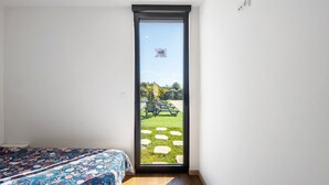 Une chambre à coucher avec un lit, une porte-fenêtre coulissante donnant sur une terrasse avec une pelouse et du mobilier d’extérieur.