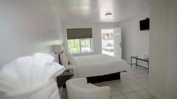 A hotel room with a bed, a chair, a small table, a window, and a door leading outside.