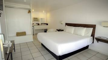 Habitación de hotel con una cama grande, un escritorio, una silla, una mesita, un espejo y un baño con lavamanos e inodoro.