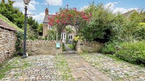A cobblestone pathway leading to a stone house with a traditional roof, surrounded by lush greenery and flowering plants. - 3 bedroom accommodation in Sutton Benger, near Lacock (Sutton Benger, near Lacock)