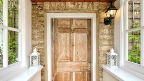 A rustic wooden door with a metal latch, flanked by two white lanterns on either side, set against a stone wall with a wooden ceiling above. - 3 bedroom accommodation in Sutton Benger, near Lacock (Sutton Benger, near Lacock)